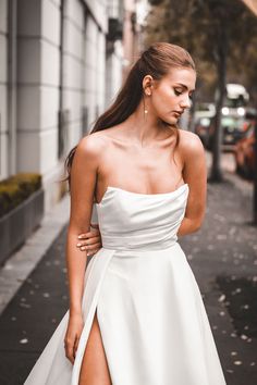 a woman in a white dress is walking down the street with her leg slited