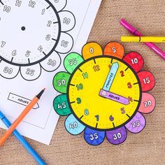 a clock with numbers on it next to colored markers and pencils, along with a coloring book