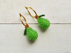 green beaded fruit earrings with gold hooks on white wooden background, close up view