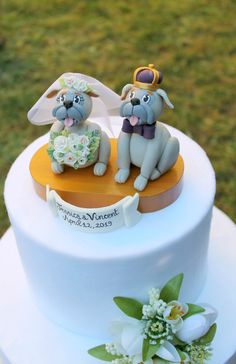 two dogs sitting on top of a white cake covered in fondant and flowers,