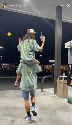 a man holding a child in his arms while he plays with an orange ball at the gas station