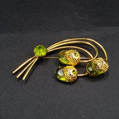 "*Description: This is a beautiful Sarah Coventry brooch entitled \"Touch of Elegance\" which has three green Austrian crystal faceted oval stones with gold tone filigree flower tops from the 1970s. Each flower top has a green rhinestone chaton with a larger green rhinestone chaton placed on the stems. This brooch is a book piece and is found on page 100 of Sarah Coventry Jewelry by Kay Oshel. The brooch is also featured in The Art of Juliana Jewelry by Katerina Musetti. This would be a great ad Antique Green Brooch For Evening, Mid-century Green Brooch For Formal Occasions, Mid-century Green Brooches For Formal Occasions, Antique Green Brooch For Anniversary, Vintage Green Brooch For Evening, Antique Green Brooches For Anniversary, Vintage Green Evening Brooch, Vintage Green Evening Brooches, Green Mid-century Style Brooches For Formal Occasions