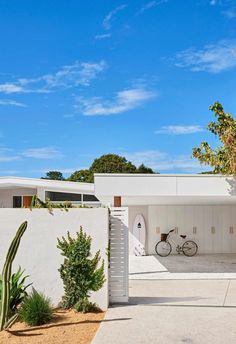 a white house with a bike parked in the driveway and cactus growing on the side