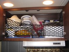 a kitchen cabinet filled with dishes and pans on top of a microwave burner