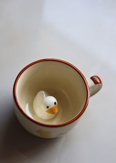 a ceramic duck in a cup on a white table top with orange trimmings