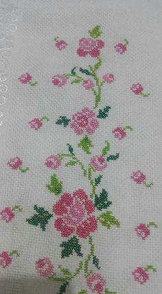 a cross stitch pattern with pink flowers and green leaves on a white table cloth,