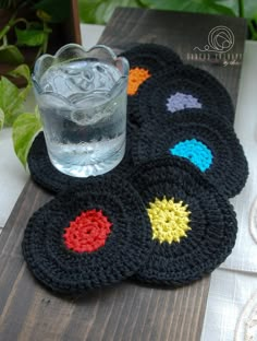 four crocheted coasters on a table with a glass of water in the middle