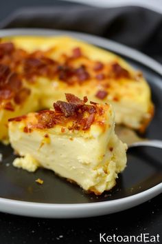 a piece of cheese and bacon quiche on a black plate with a silver fork