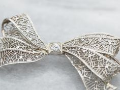 Add a touch of elegance and whimsy to any outfit with this bow brooch. The delicate filigree detailing and sparkling European Cut diamond make this brooch a timeless statement piece. Perfect for any occasion!Metal: 14K White GoldGem: European Cut Diamond .10 Carats, SI1 in Clarity, I in ColorGem Measurements: 3.2 mm, RoundMeasurements: 44 x 23 mmMarks: "X14K" Stamped on the pin guard Elegant White Gold Brooches For Evening, Elegant White Gold Evening Brooches, Exquisite Diamond Accented Brooches For Wedding, Exquisite Wedding Brooches With Diamond Accents, Elegant Anniversary Brooch With Bow, Diamond Filigree Brooches As Gift, Elegant Brooch With Diamond Accents As Gift, Elegant Diamond Accented Brooch Gift, Elegant Diamond Accented Brooches As Gifts