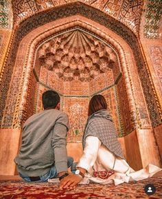 two people sitting on the floor in front of an intricately decorated wall and ceiling