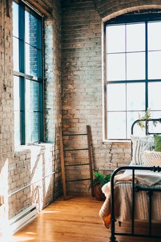 a bedroom with a brick wall and wooden flooring next to a bed in front of a window