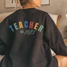 TEACHER EST. 2021 printed on the back is the perfect graduation gift or present for yourself for doing so well! Perfect for NEW graduate teachers everywhere! It fits like a well-loved favorite. Comfortable during your long days x You'll also love our super-soft shirts durability and with our direct-to-garment printing, it means no cracking, peeling or fading. Shirts age gracefully so you can enjoy your garment for years to come. SIZING - This sweatshirt is technically UNISEX sizing - this is pri Black Tops For College End Of School Year, Relaxed Fit T-shirt For College, Back To School, Black Text Print Top For Back To School, School Spirit Tops For Back To School Teaching, Back To School Slogan Tops For College, Slogan Tops For College And Back To School, Slogan Tops For College Back To School, Back To School Spirit Tops For Teaching, School Spirit Top With Slogan For Teacher Appreciation