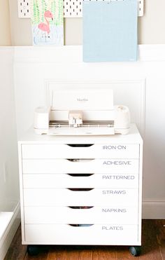 a white dresser with five drawers and pictures on the wall