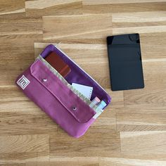 a purple bag sitting on top of a wooden floor next to a cell phone and wallet