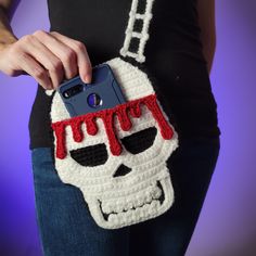 a woman holding a cell phone case with a crocheted skull on the front