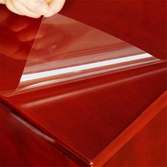 a person holding a piece of clear plastic in front of a wooden table with red furniture