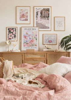 an unmade bed with pink linens and pictures on the wall above it in a bedroom