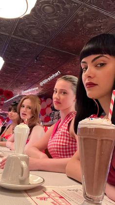 three women are sitting at a table with drinks in front of them and one woman is looking off to the side