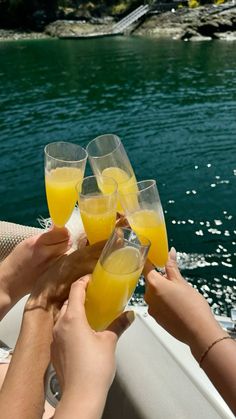 four people toasting with glasses of orange juice on a boat in the water,