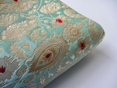 a close up view of a blue and gold pillow with red flowers on the side