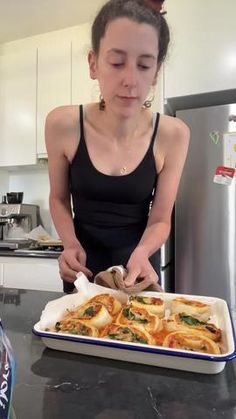 a woman standing in front of a pan filled with food on top of a counter