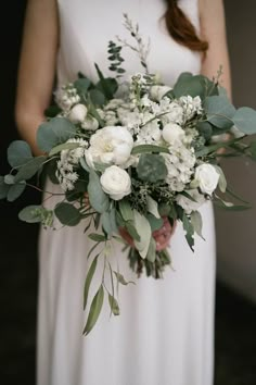 a woman holding a bouquet of white flowers and greenery on her wedding day is instagraming