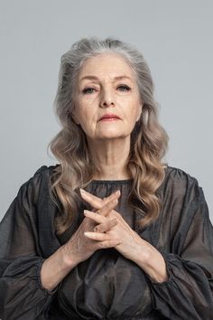 an older woman with grey hair and black dress is holding her hands together in prayer