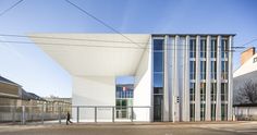 a person walking on the street in front of a white building with glass walls and metal railings