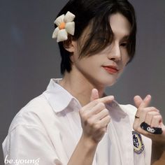 a woman with a flower in her hair is making a hand gesture while wearing a white shirt