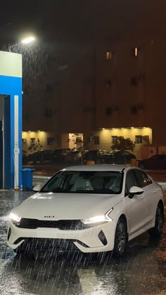 a white car is parked in front of a gas station with rain coming down on it