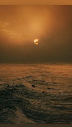 the sun is setting over the ocean with surfers in the water on their surfboards