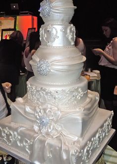 a large white wedding cake sitting on top of a table next to other people at a party