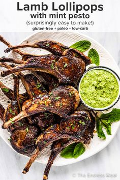 grilled lamb chops on a white plate with green dipping sauce and mint leaves