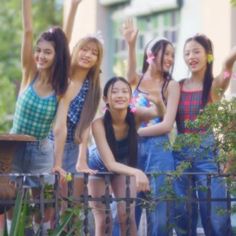 group of young women standing next to each other in front of a fence and trees