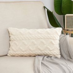 a white pillow sitting on top of a couch next to a green leafy plant