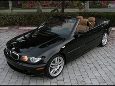 a black convertible car parked on top of a brick road next to bushes and trees