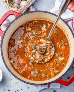 a ladle full of soup with meatballs in it and garlic on the side