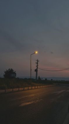 an empty street at night with the sun setting in the distance and telephone poles on either side