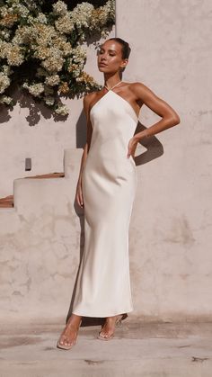 a woman standing in front of a wall wearing a white dress with one shoulder cut out