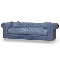 a blue couch with buttons on the back and arms, sitting in front of a white background