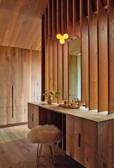 a bathroom with wooden walls and flooring has a vanity, stools, and mirror