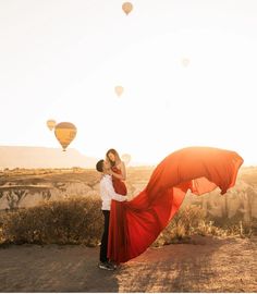 a man and woman standing in the desert with hot air balloons flying above their heads