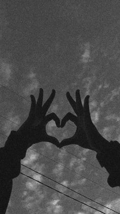 two hands in the shape of a heart against a cloudy sky with power lines and telephone poles