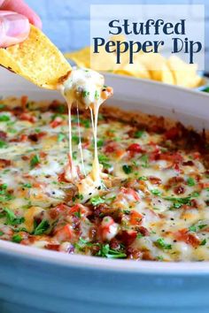 a hand holding a tortilla chip and dipping it into a casserole dish