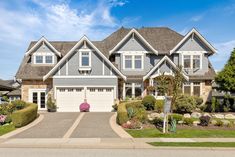 a large house with lots of windows and landscaping on the front lawn, along with two driveways