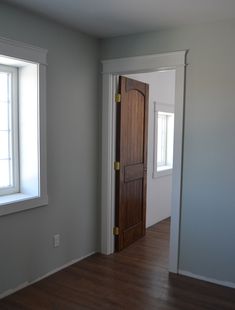 an empty room with a wooden door and hard wood flooring in front of two windows