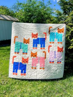 a quilt made to look like cats on the grass in front of a tree and fence