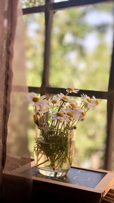 a vase filled with white and yellow flowers on top of a wooden table next to a window