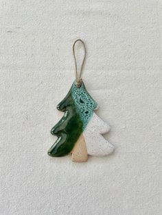 a ceramic ornament hanging from a cord on a white surface with a green tree