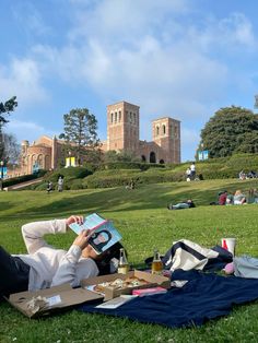 a person laying on the grass reading a book and drinking some beer in front of a castle